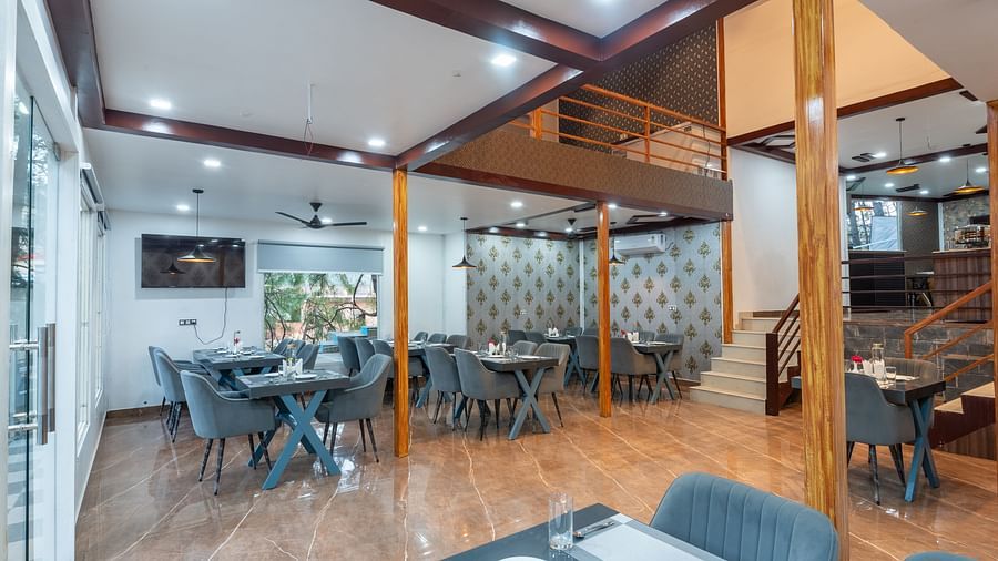 Elegant restaurant interior with grey upholstered seating, set dining tables, tiled flooring, and decorative wallpaper near a staircase - DLS Nature Trinket Resort, Dalhousie.
