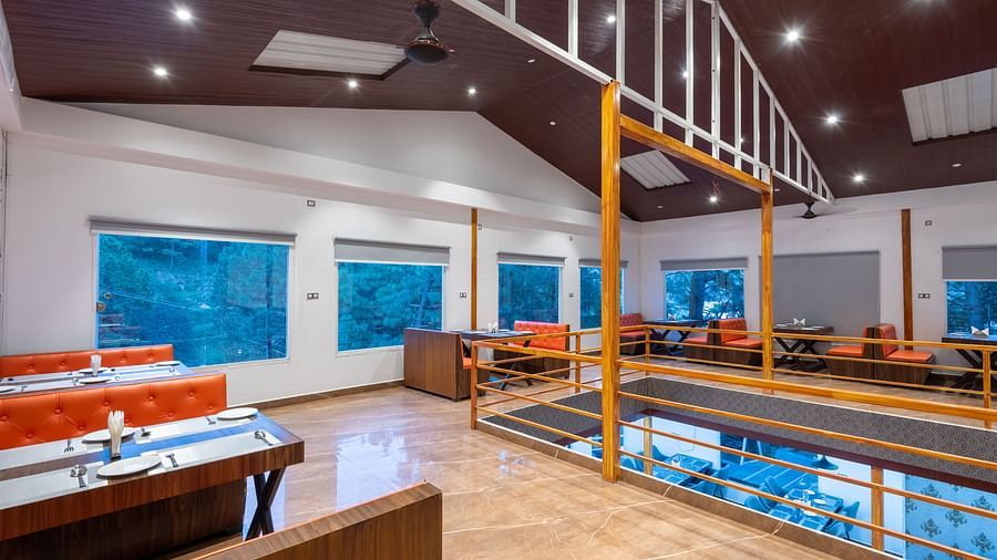 Modern restaurant interior with wooden furniture, orange seating, large windows, and ceiling lights - DLS Nature Trinket Resort, Dalhousie.