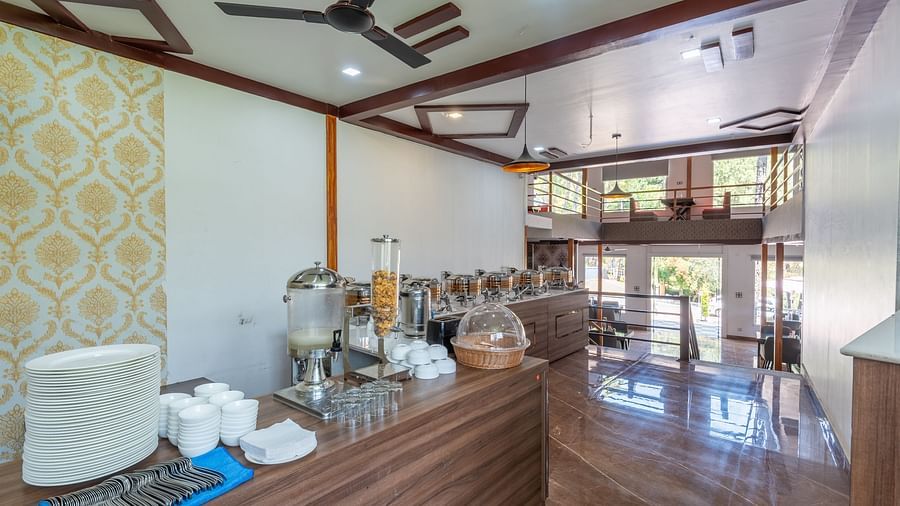 Restaurant buffet counter with serving containers, utensils, and modern decor featuring wood finishes and patterned wallpaper - DLS Nature Trinket Resort, Dalhousie.