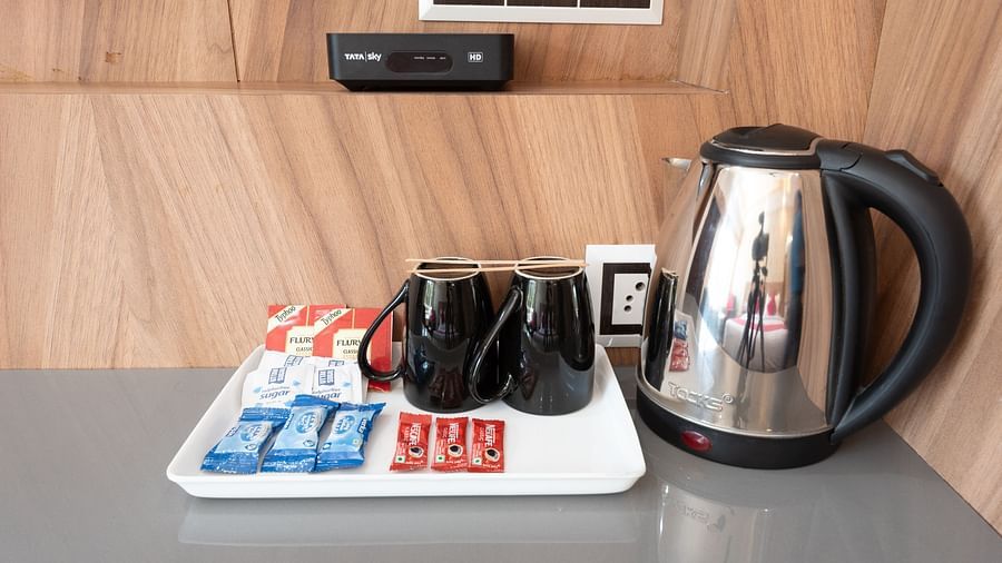  Hospitality tray with two black mugs, sachets of tea, coffee, and sugar, along with milk portions, placed beside a stainless steel electric kettle on a countertop - DLS Nature Trinket Resort, Dalhousie.