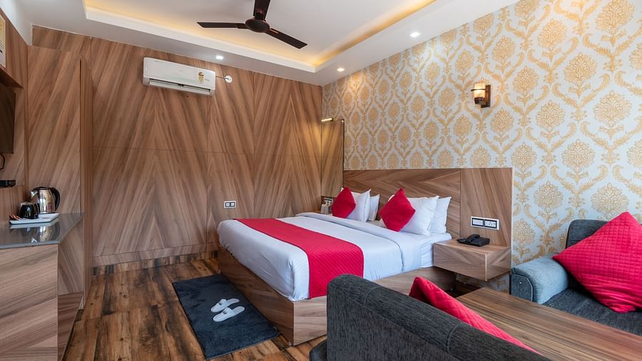 Modern hotel room with wooden interiors, a double bed featuring red accents, stylish wallpaper, a sitting area, and an electric kettle station - DLS Nature Trinket Resort, Dalhousie.