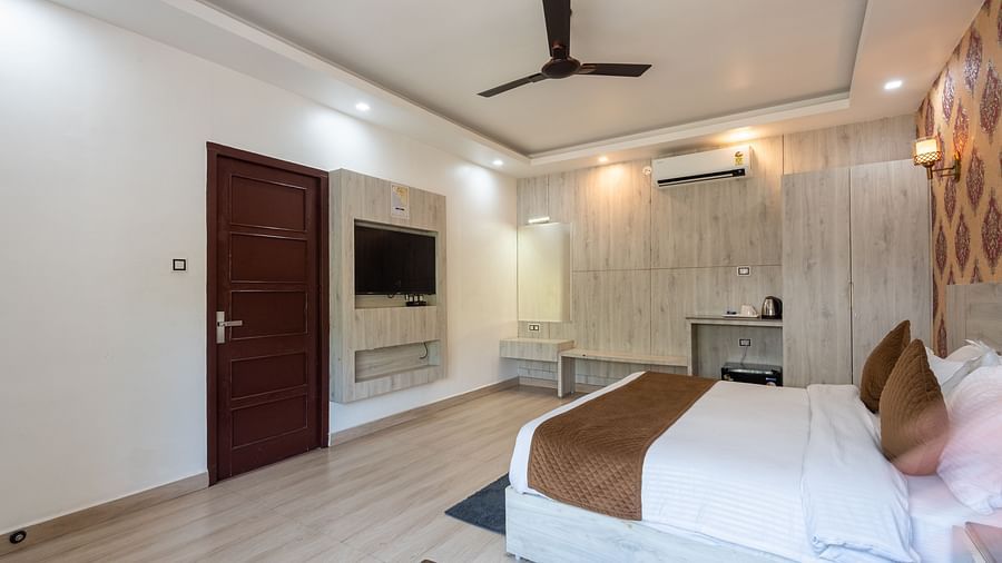 pacious hotel room with a large double bed, brown and cream décor, wall-mounted television, ceiling fan, air-conditioning unit, and a small desk area - DLS Nature Trinket Resort, Dalhousie.