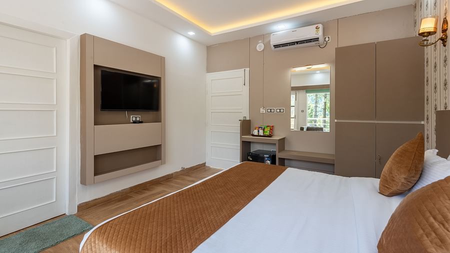 Modern hotel room interior with a neatly made bed, wall-mounted flat-screen TV, vanity area with mirror, air conditioning, and warm ambient lighting - DLS Nature Trinket Resort, Dalhousie.