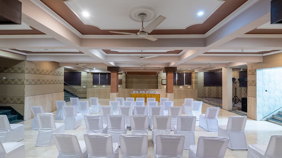 A banquet hall with chairs arranged for guests, featuring a ceiling fan, captured from the back at DLS Park Grace, Haridwar.