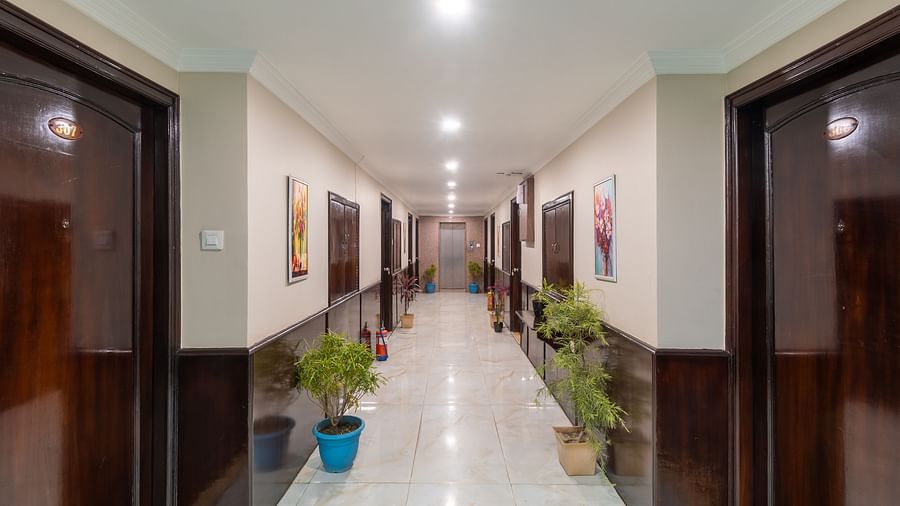 Corridor area at DLS Park Grace, Haridwar featuring multiple wooden doors, potted plants and bright lights.