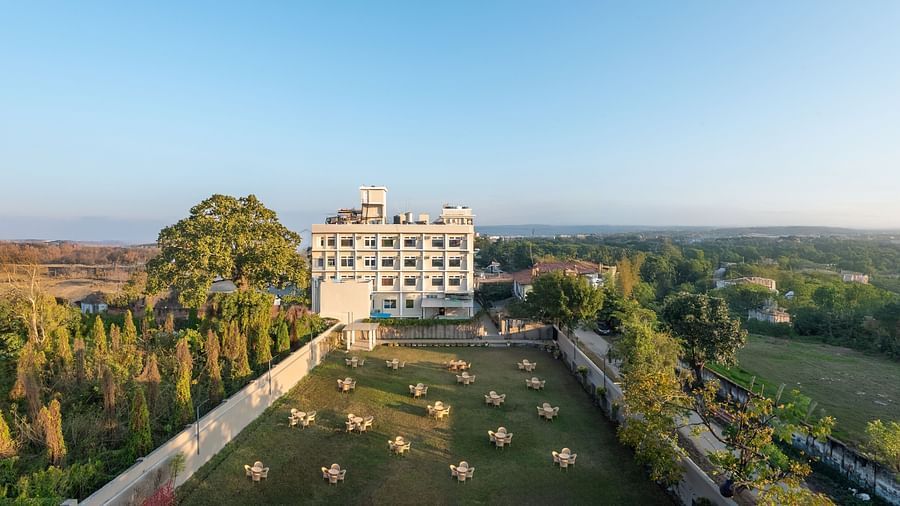  Lawn area at DLS Park Grace, Haridwar featuring several sets of tables and chairs surrounded by luscious green trees and site of the clear blue sky.
