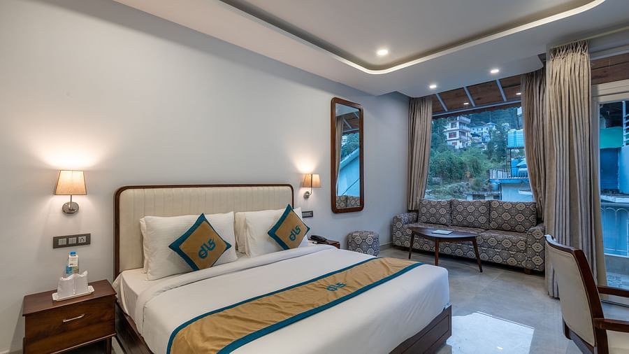 A Deluxe Non view room at DLS Spring Valley resort  Dharamshala featuring a  king bed, table, chairs and a big window