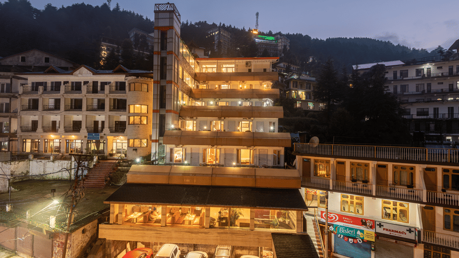 Exterior facade view of DLS Spring Valley Resort, Dharamshala, featuring bright lighting and a car parking area below.