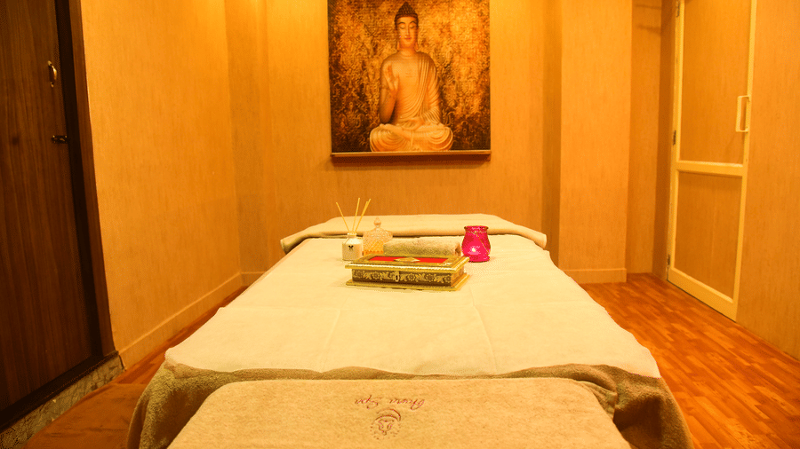 A serene spa treatment room at DNC Shevaroys Resort & Spa with a massage bed, warm lighting, and a Buddha painting on the wall.