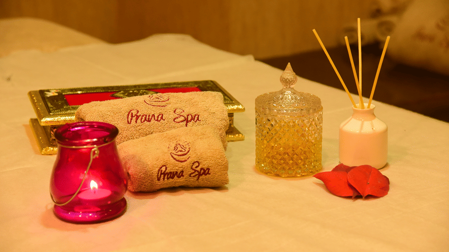 Close-up of spa amenities at DNC Shevaroys Resort & Spa, featuring rolled towels, a candle holder, and a reed diffuser on a massage bed.