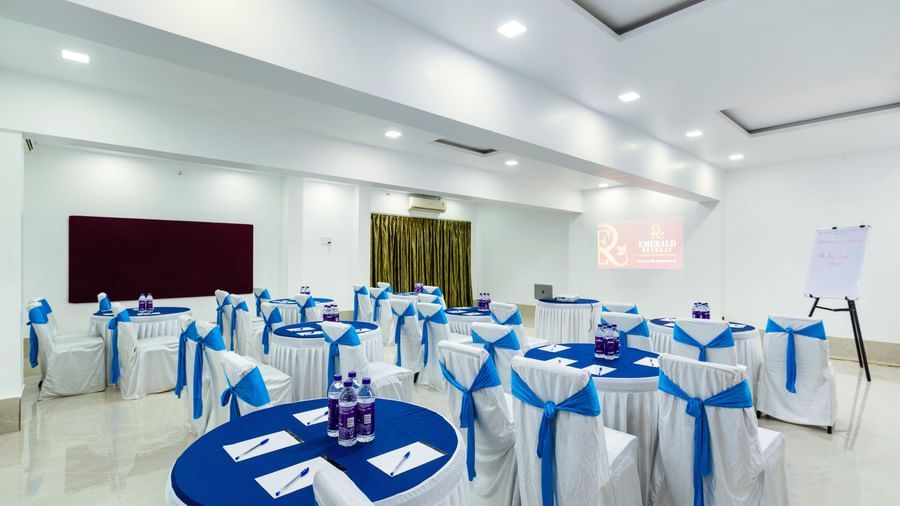 Banquet hall with round tables and blue-themed event setup at Emerald Retreat, Tungarli.