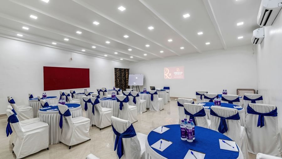 Banquet space with white chairs and blue round table arranged in cluster setting at Emerald Retreat, Tungarli.
