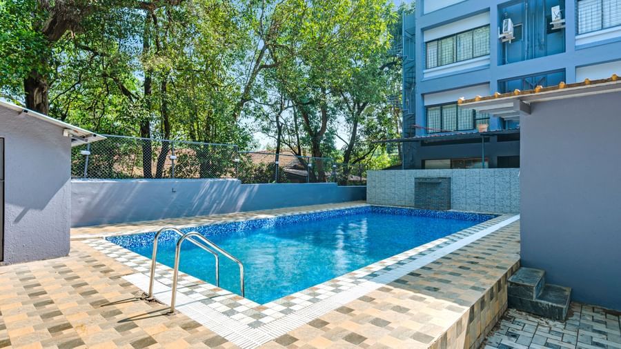 Outdoor swimming pool surrounded by trees and tiled flooring at Emerald Retreat, Tungarli.
