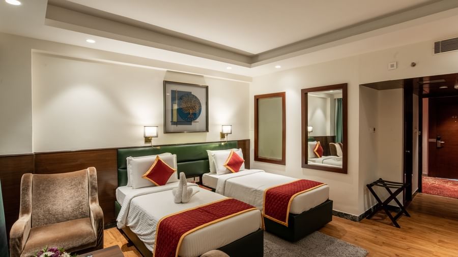 Twin bedroom with stylish decor, armchair, and framed artwork at Hotel Royal Regency Chennai