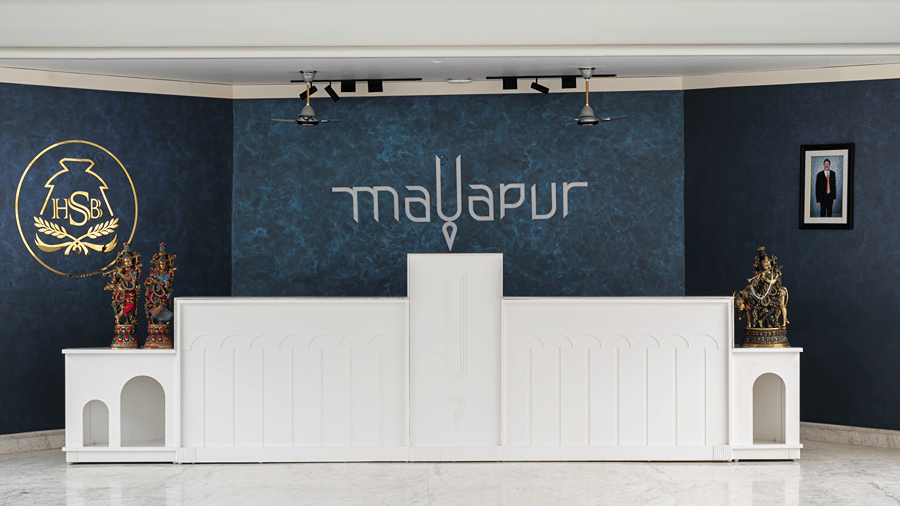 A front desk counter at Hotel Sonar Bangla, Mayapur, featuring a wall logo, decorative idols, and spotlight fixtures.
