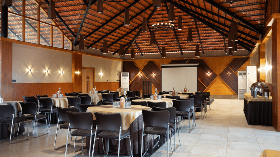 Interior view of a large banquet hall with a high wooden ceiling, round tables with gold tablecloths, and black chairs at Hotel Sonar Bangla, Sundarban.