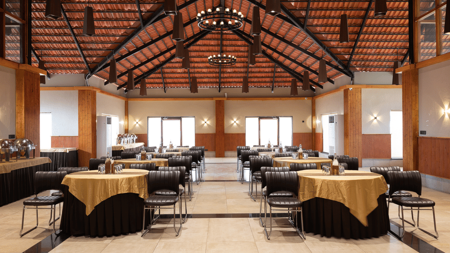 Wide shot of a banqet hall featuring multiple round tables and a high vaulted wooden roof at Hotel Sonar Bangla, Sundarban.