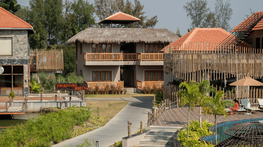 Exterior shot of resort buildings with thatched roofs and stone walls connected by a paved pathway at Hotel Sonar Bangla, Sundarban.