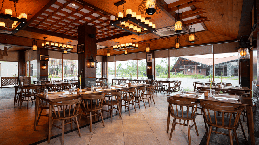 Spacious dining hall with multiple wooden tables, warm ceiling lighting, and tiled flooring at Hotel Sonar Bangla, Sundarban.