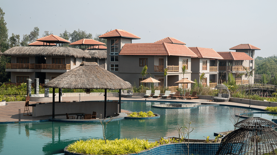 Large outdoor swimming pool with a chaise lounges and various multi-storey hotel buildings with red roofs in the background at Hotel Sonar Bangla, Sundarban.