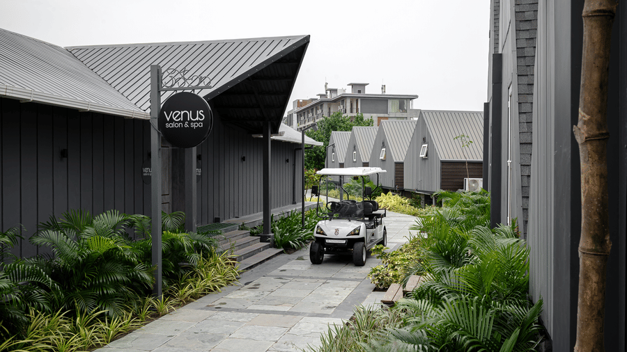 A driveway leading past A-frame cottages, with a golf cart parked on the side at Hotel Sonar Bangla, Taki.