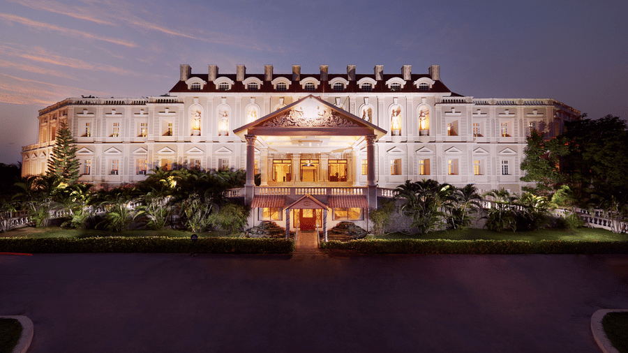 The grand illuminated exterior facade of the hotel building at dusk with a manicured driveway - Jenneys Residency, Coimbatore