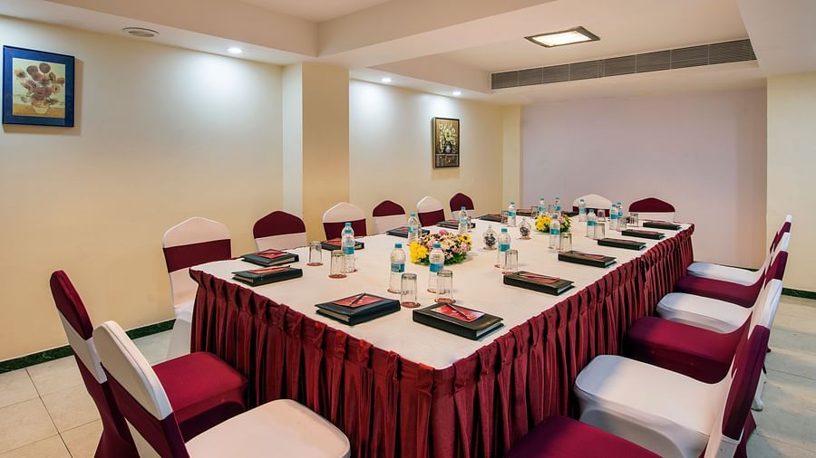 A formal dining room is set with a long table covered in a red patterned cloth, surrounded by chairs - Lords Inn Vadodara