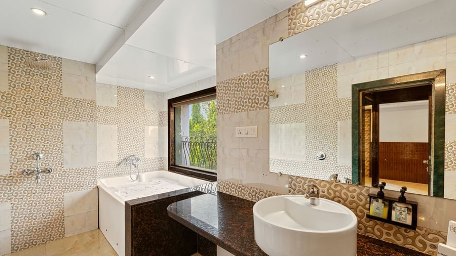 Contemporary bathroom with a wide mirror, wash basin, a large bathtub, and beige tiled walls at Mayur Retreat.
