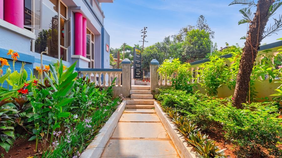 A pathway at Mayur Retreat surrounded by plants and trees, besides the hotel building.