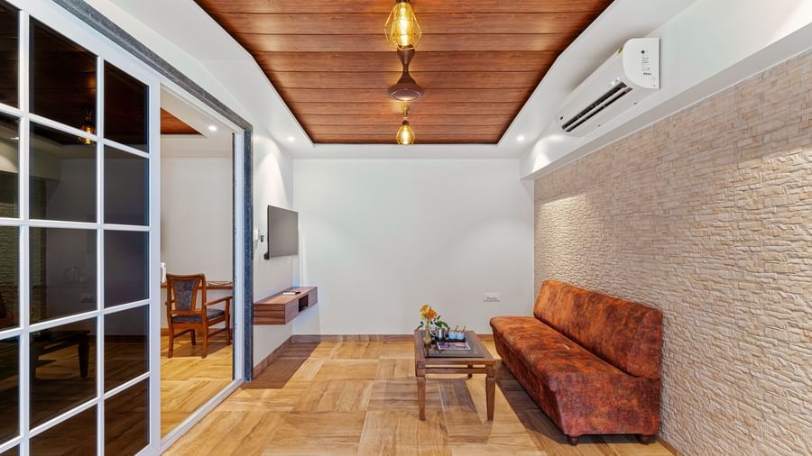 Sitting area at Mayur Retreat with a wooden bench and textured walls, adjoining a bedroom via glass sliding doors.