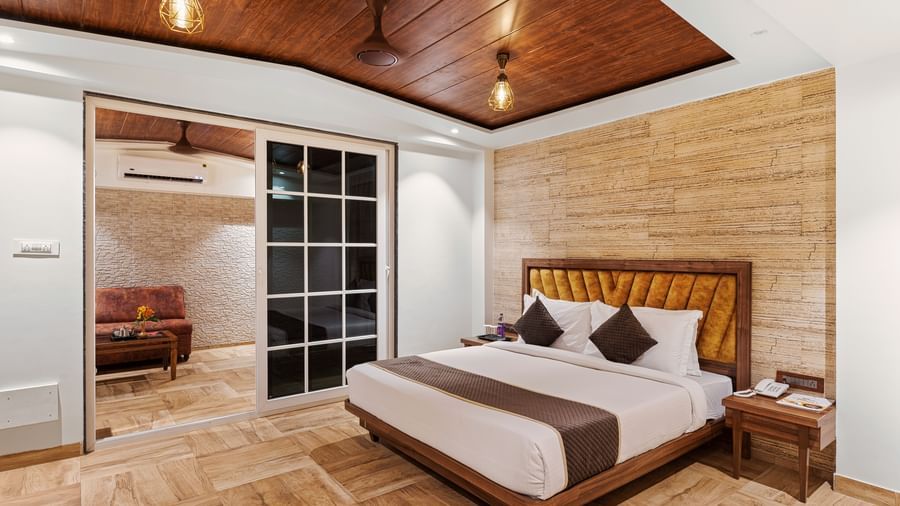 Cosy bedroom at Mayur Retreat featuring a double bed, wooden ceiling, warm lighting, and sliding glass doors opening to a balcony.