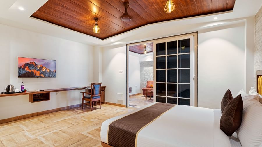 Spacious room at Mayur Retreat with a large bed, wall-mounted TV, and wood-accented ceiling, designed for comfort and relaxation.