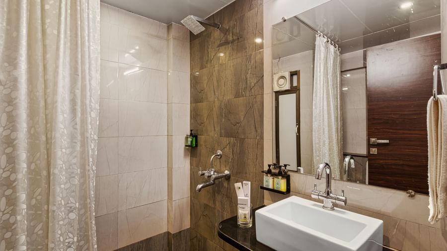 Modern bathroom at Mayur Retreat with beige tiling, glass shower partition, and a wash basin.