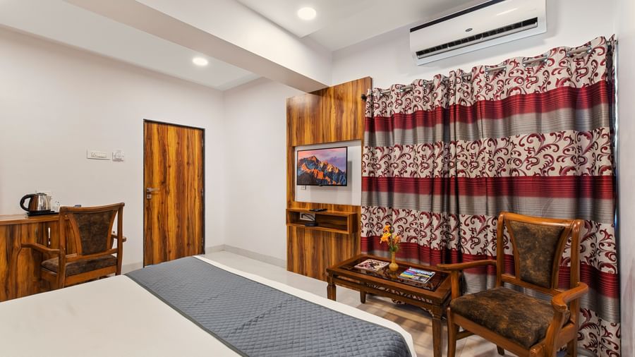 Traditional-style room at Mayur Retreat with wooden furniture, patterned curtains, and a grey bedspread.