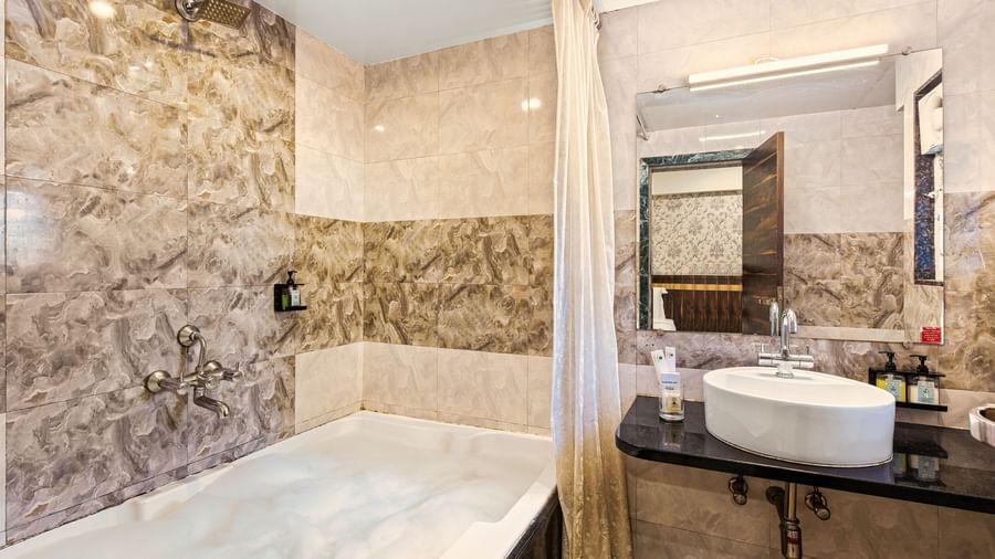 Modern bathroom at Mayur Retreat with a bathtub, stone-textured walls, and a large mirror.
