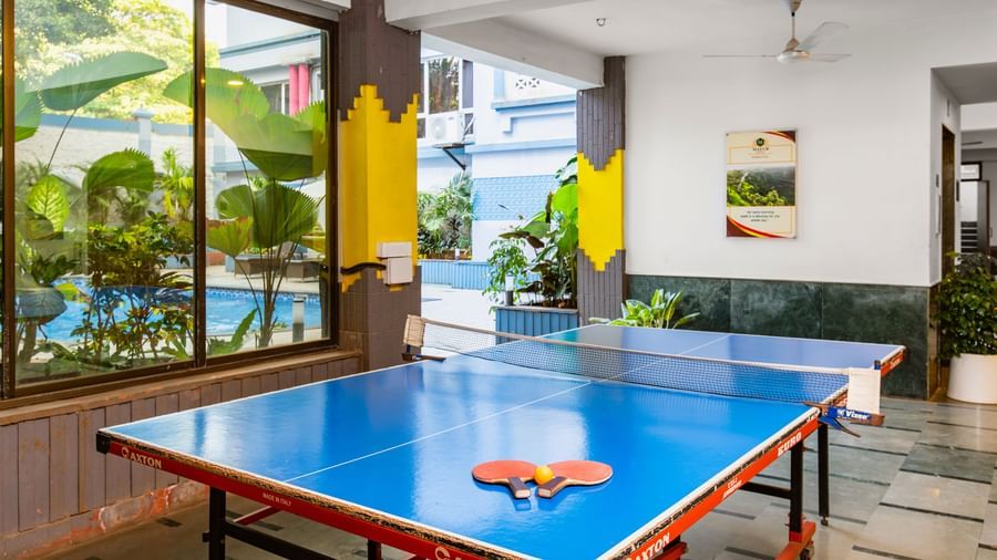 Indoor recreational room at Mayur Retreat featuring a table tennis setup, potted plants, and glass walls offering a mix of fun and relaxation in a lively environment.