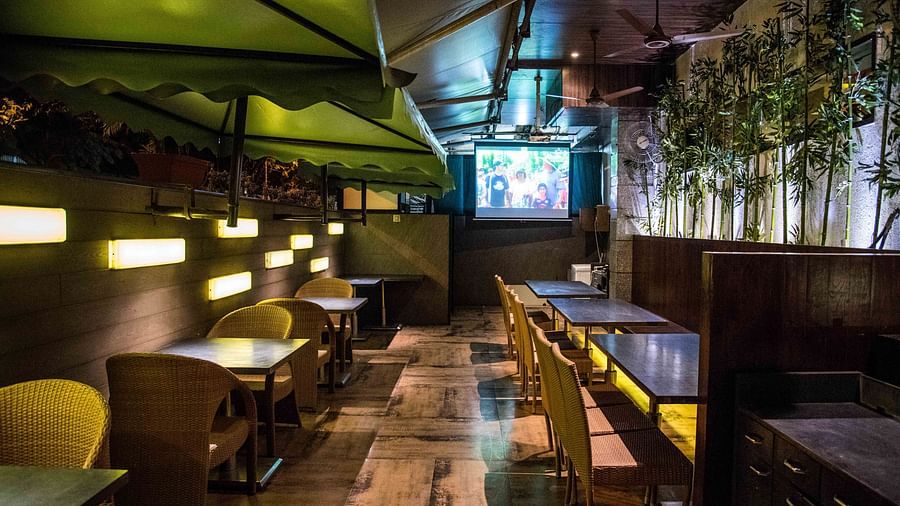 Modern restaurant featuring wooden chairs, tables, and a wall with plants hanging as decoration at Oriental Aster, Mumbai.