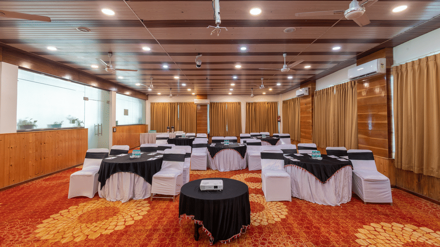Well lit banquet hall at DLS Hotels On The Ganges with circular tables and chairs surrounding them.