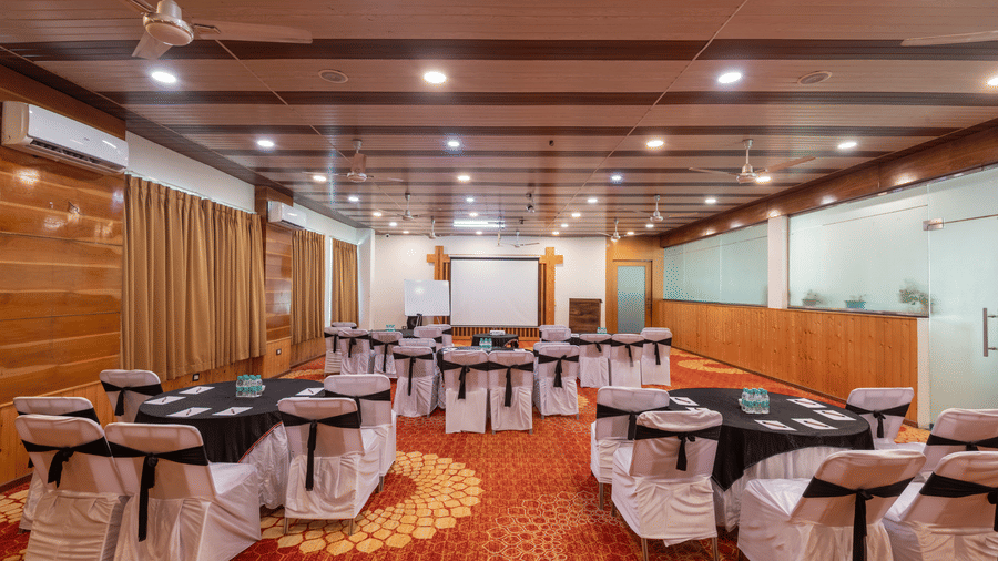 Bright banquet hall with tables and chairs om decorative orange rug at DLS Hotels On The Ganges.