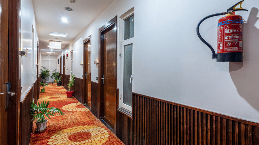 Corridor with wooden doors, potted plants and orange carpet at DLS Hotels On The Ganges.