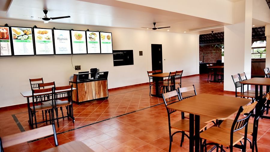 A diagonal view of the dining area at Riverside Inn with tables, chairs, a ceiling fan, and high-level windows.
