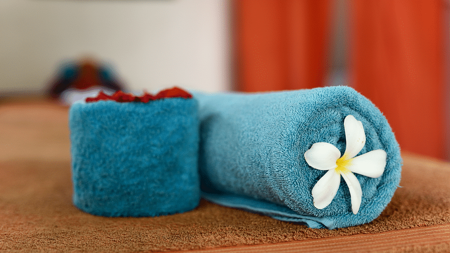 A neatly rolled blue towel with a delicate white flower resting on top, placed on a wooden surface at Shooting Star Boutique Hotel