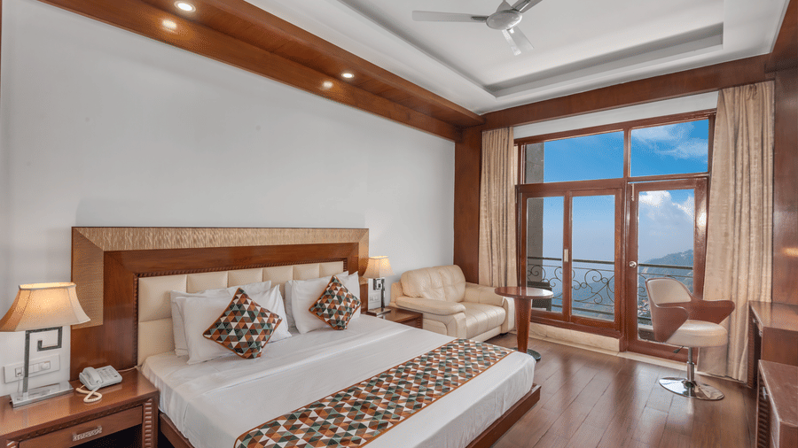 Comfortable bedroom with plush double bed, warm lighting, and scenic balcony view at The Solitaire Resort, providing a peaceful stay with homely interiors.