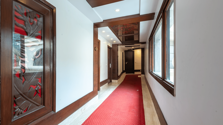 A bright corridor with glass windows, red carpet flooring, and wooden detailing leading to rooms at The Solitaire Resort.