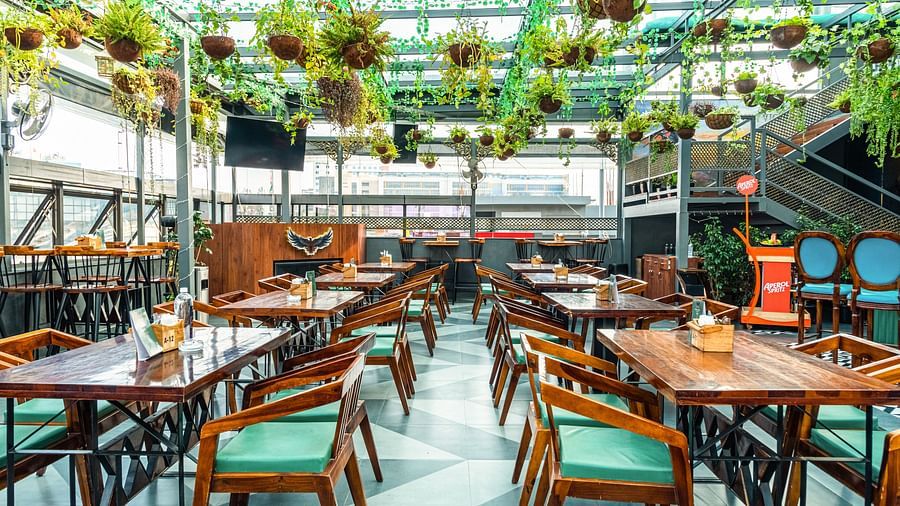 With plants hanging from the roof and wooden chairs with green cushions at Kyba restaurant at Visthara - Urban Boutique Hotel 10