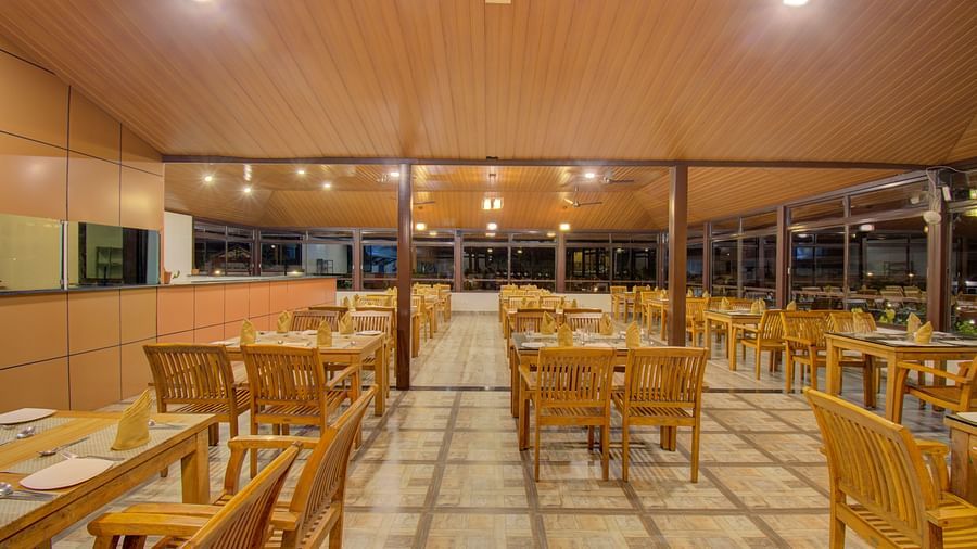A spacious dining area with wooden tables and chairs, illuminated by warm lighting | Sheesham Restaurant | Woodstock Resorts, Coorg