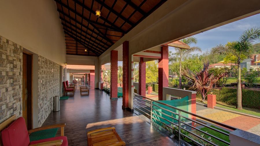A tiled balcony with chairs that overlooks the main passage and greenery | Woodstock Resorts, Coorg