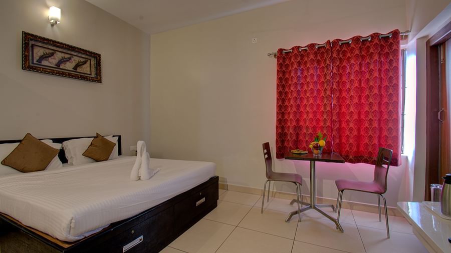 a Swan made of towel on a huge bed, table, chairs, and windows with curtains | Superior Room | Woodstock Resorts, Coorg
