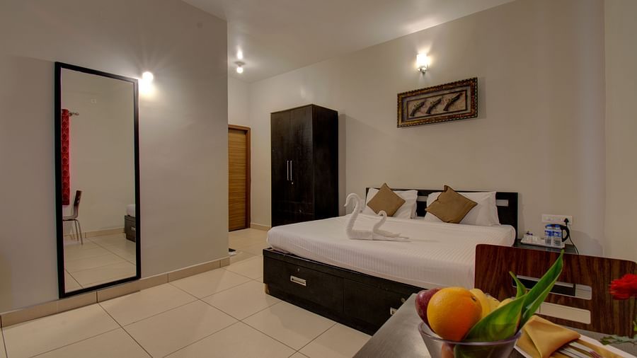 A bedroom with a huge bed, a mirror, Cupboard, a table with fruits on it | Superior Room | Woodstock Resorts, coorg