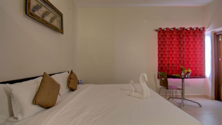 Bedroom with a swan made with towel on a large bed, table, chair, curtained window | Superior Room | Woodstock Resorts, Coorg